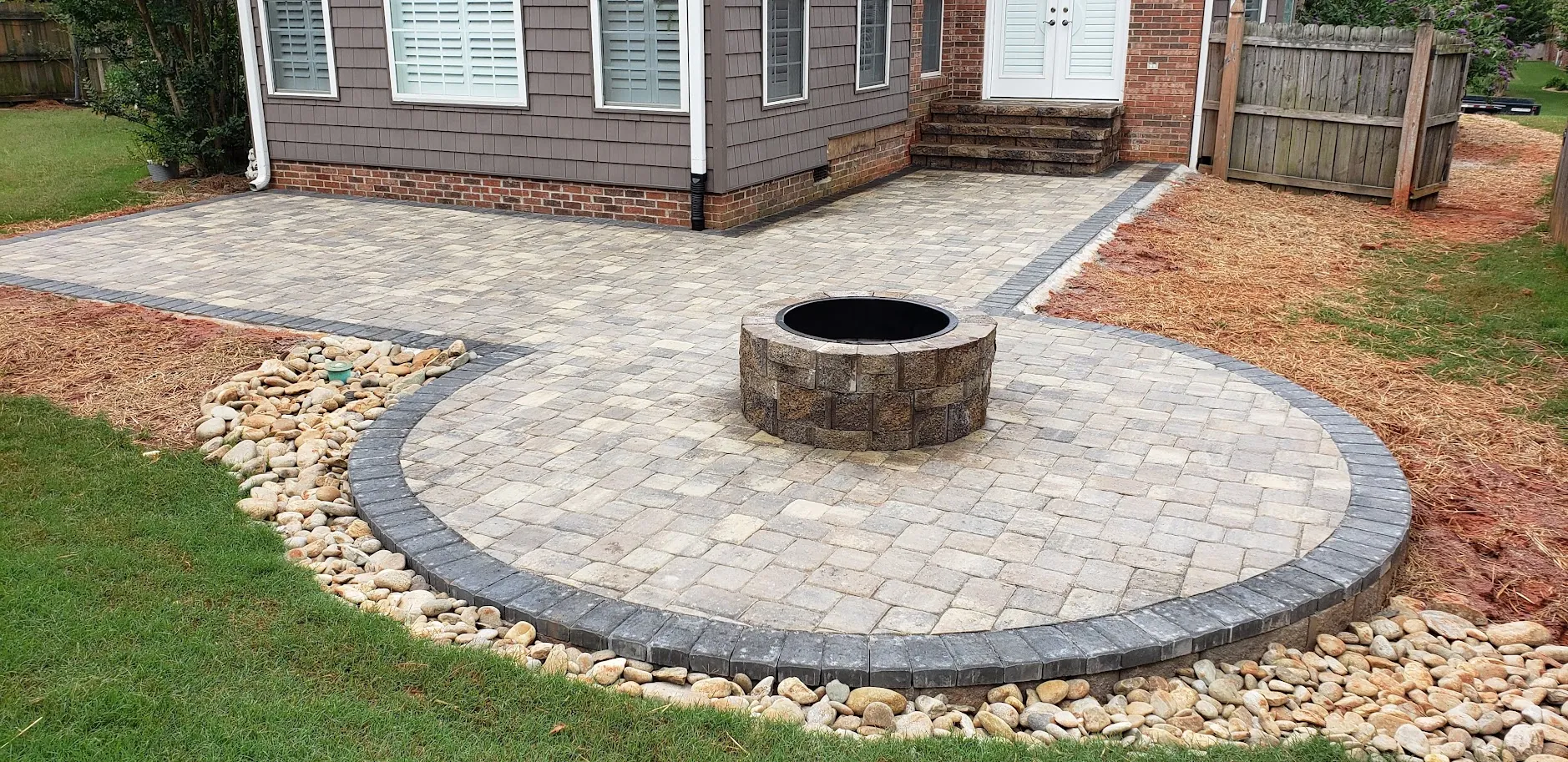 Circular paver patio with a built-in fire pit, bordered by a river-rock drainage edge