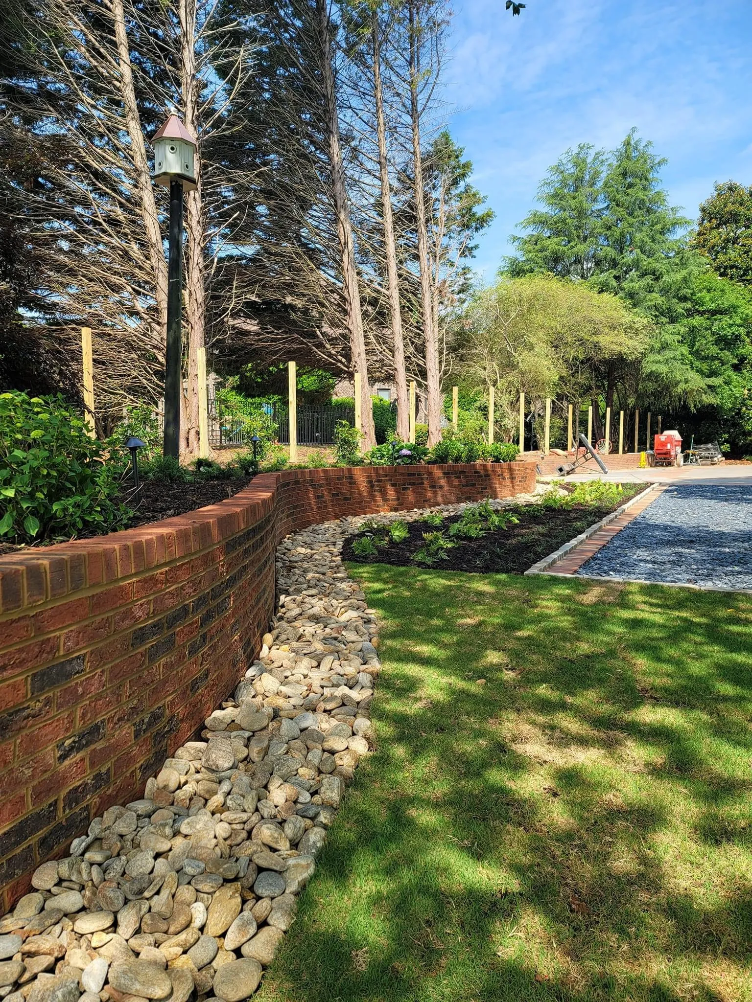 Curving brick retaining wall with a river-rock drainage border and freshly planted landscape bed